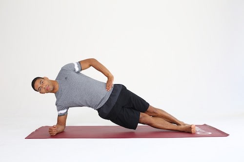 Mann macht seitlichen Unterarmstütz die Übunge Side Plank auf roter Trainingsmatte -Plank Varianten