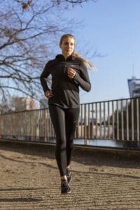 Frau beim Lauftraining in Laufkleidung joggt am Wasser.
