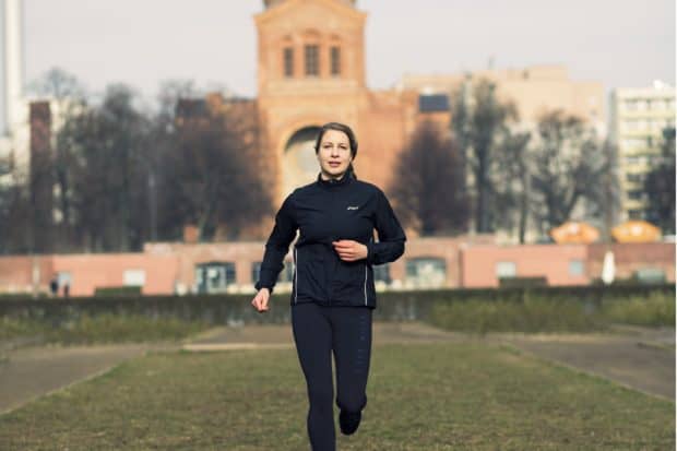 Junge Frau in schwarzer Funktionskleidung joggt durch den Park