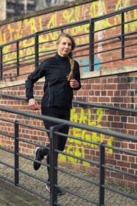 Junge Frau in schwarzer Funktionskleidung joggt eine Steigung hoch