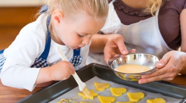 Kind bestreicht gelbe Plätzchen in Herzform