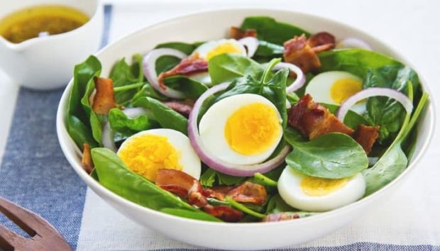 Eierscheiben mit jungem Spinat und Baconscheiben in weißer Keramikschüssel