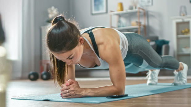 Strong woman doing plank on forearms in her cozy living room.