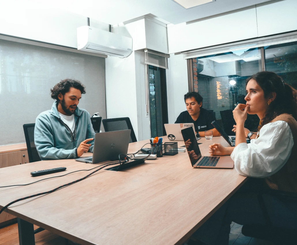 Three people seated around a conference table collaborating with laptops in a modern office.