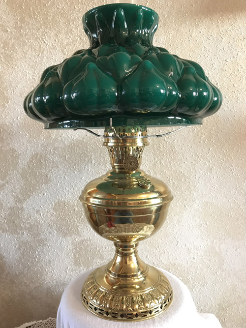 Vintage brass oil lamp with an ornate base and a green glass shade on a white cloth.