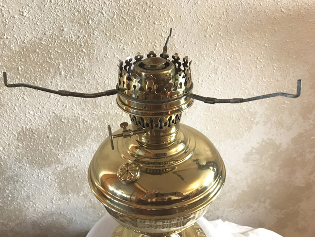 Close-up of a shiny brass antique oil lamp burner with adjustable wick knob and metal arm supports.