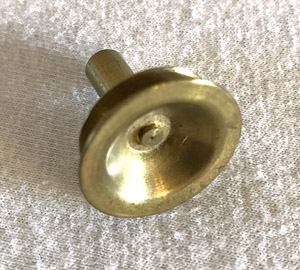 Close-up of a small round brass cabinet knob on a textured beige surface.
