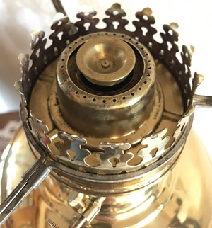 Close-up of brass oil lamp burner with decorative perforated crown and wick adjuster.