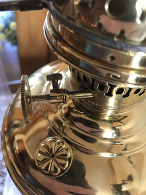 Close-up of a shiny vintage brass oil lamp with a focusing knob and decorative details.