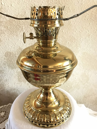 Shiny brass antique oil lamp with decorative patterns on a white cloth-covered surface.