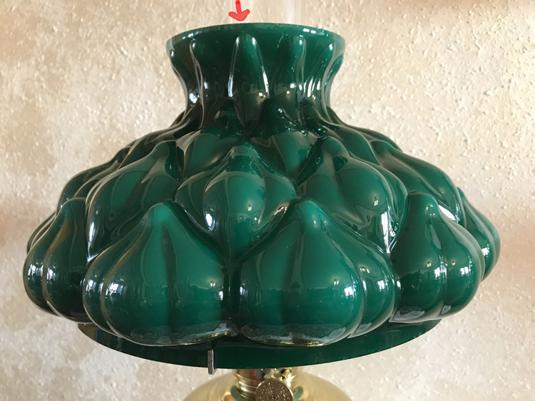 Close-up of a glossy green artichoke-shaped glass lamp shade with a red arrow drawn above the opening.