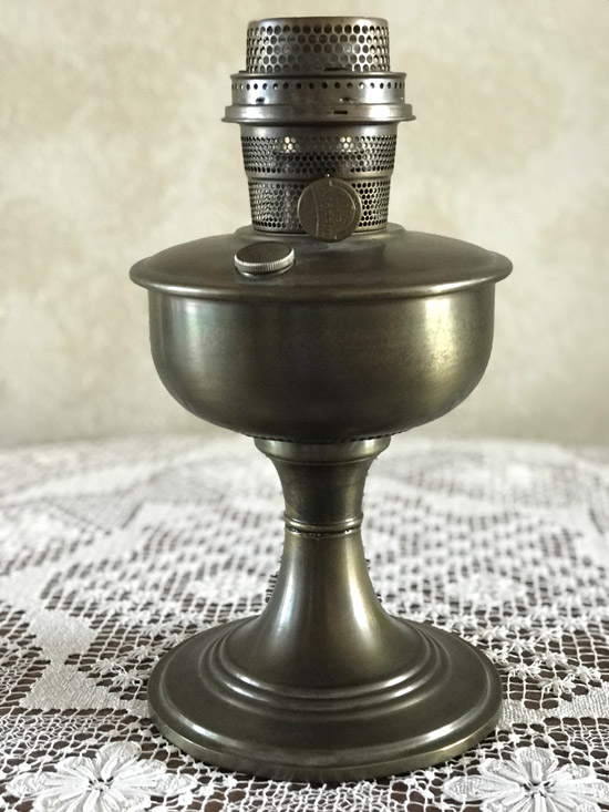 Antique bronze oil lamp with perforated top sitting on a lace tablecloth.