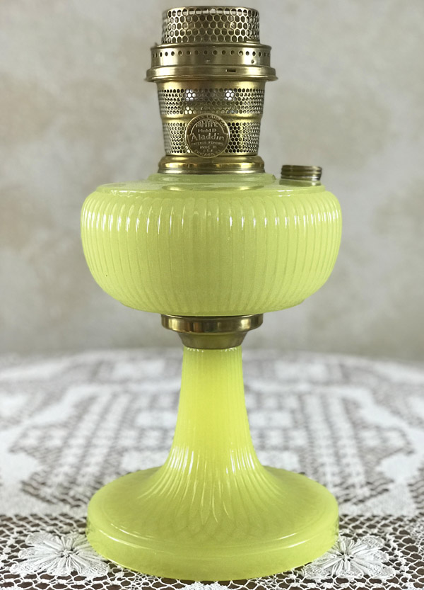 Vintage yellow glass oil lamp with brass burner sitting on a lace-covered table.
