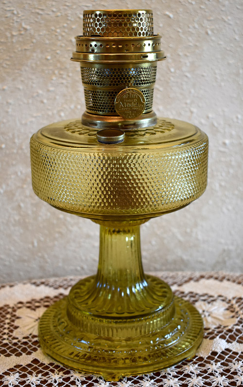 Vintage amber glass Aladdin oil lamp with metal burner on lace cloth.