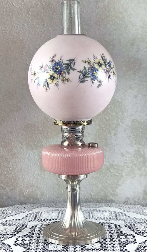 Vintage pink glass oil lamp with floral designs on globe and a silver pedestal base.