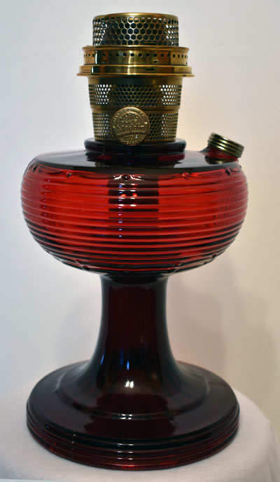 Vintage red glass oil lamp with brass burner and wick adjustment knob.
