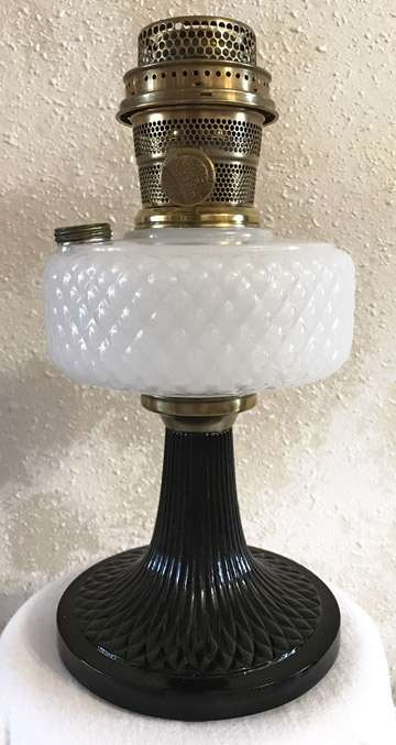 Vintage kerosene lamp with a black base, white quilted glass reservoir, and brass burner top.