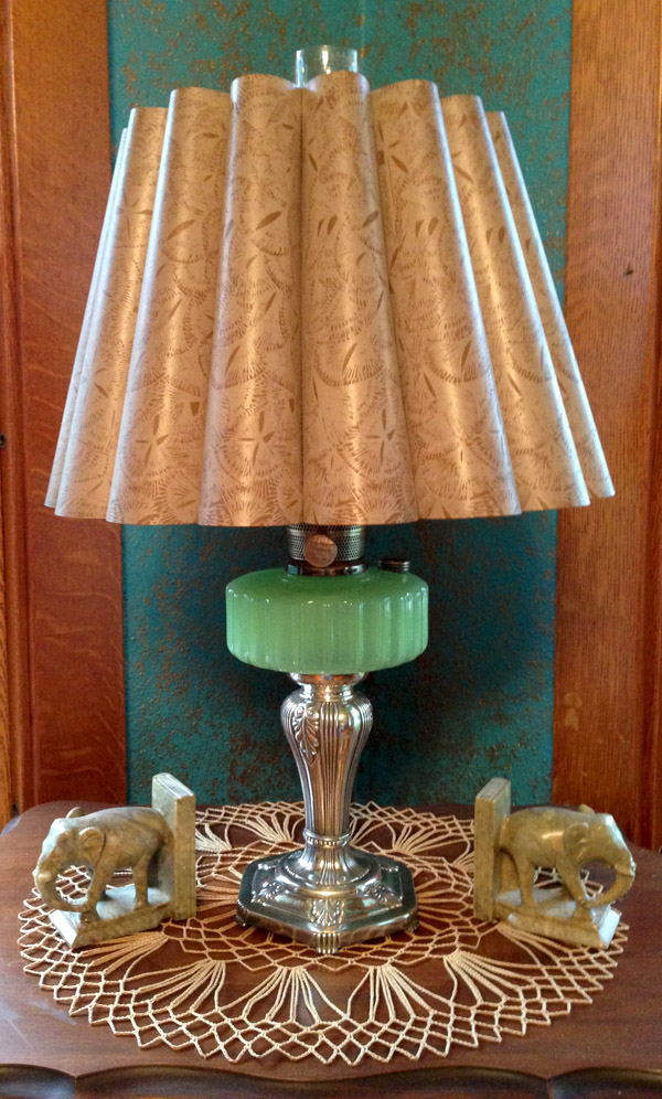 Vintage lamp with patterned beige shade, green glass base, silver stand, on lace doily with elephant bookends.