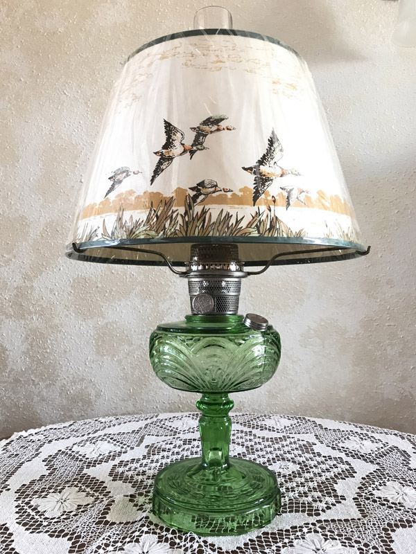 Vintage green glass oil lamp with a bird-themed lampshade on a lace tablecloth.