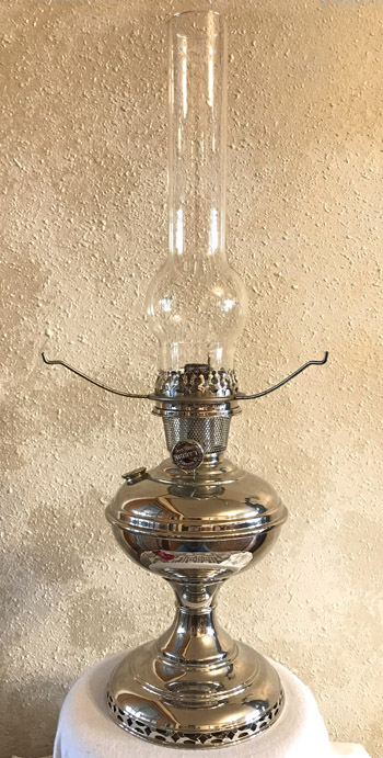 Shiny silver metal oil lamp with glass chimney on a white cloth surface.