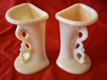 Pair of vintage milk glass bookends with ornate handles on a red fabric background.