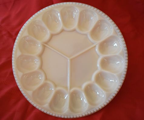 White ceramic deviled egg platter with 12 egg-shaped compartments on a red cloth.