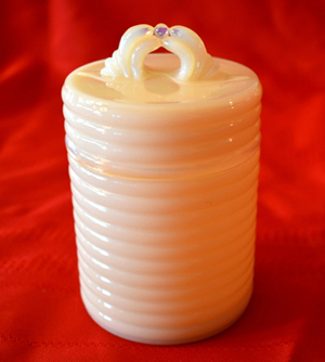 Glossy white ribbed cylindrical container with swan-shaped handles on a red fabric background.