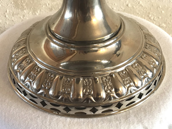 Close-up of an ornate silver base with floral and geometric cutout designs on a white surface.