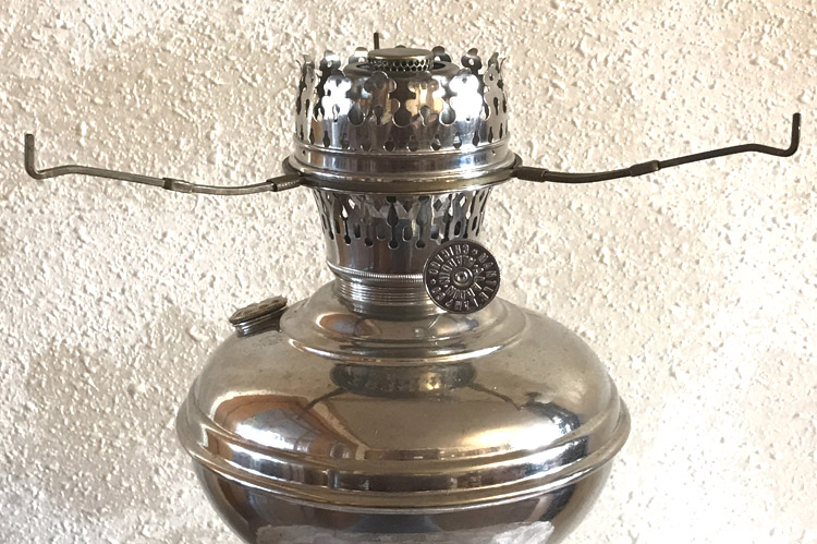 Close-up of a metallic vintage oil lamp burner with a perforated crown and adjustable knobs.