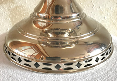 Base of a shiny metallic lamp with decorative cut-out patterns resting on a textured surface.