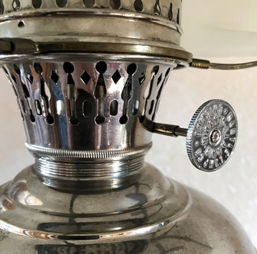 Close-up of a shiny metal lantern burner with a round adjustment knob on the side.