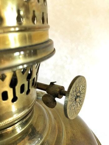 Close-up of a vintage brass kerosene lantern’s wick adjustment knob and perforated gallery.