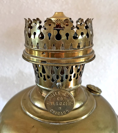 Close-up of a brass oil lamp burner top with ornate perforated crown and adjuster knob.