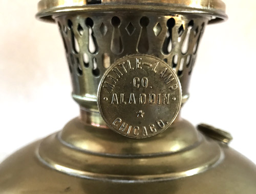 Close-up of brass Aladdin Mantle Lamp Co. Chicago emblem on an antique lamp burner.