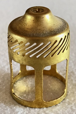 Close-up of a small, cylindrical brass object with diagonal cutouts and four vertical supports.