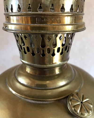 Close-up of a brass oil lamp burner with ventilation holes and 'Model No 3' inscription.