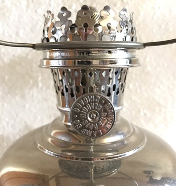 Close-up of a vintage metal oil lamp burner with perforated top and adjustment knob.