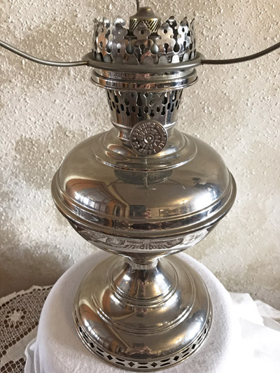 Close-up of a shiny silver antique oil lamp with perforated top and round base on a white cloth.