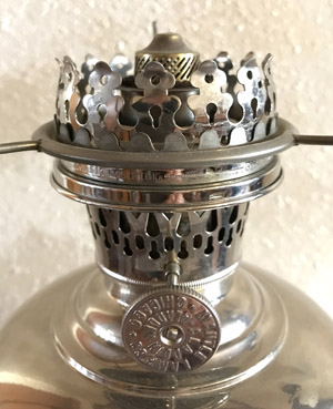 Close-up of a vintage silver oil lamp burner with ornate metalwork and adjustment knob.