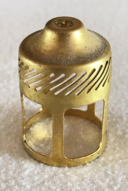 Small gold metal cylindrical object with slits and an elevated rounded top.