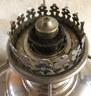 Close-up of the metal burner and wick adjustment knob on an antique oil lamp.