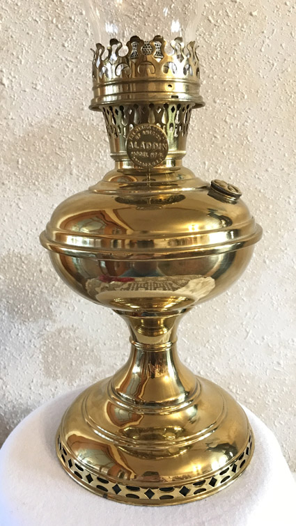 Shiny brass Aladdin model 5501 oil lamp with glass chimney on a white surface.