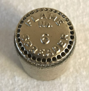 Metal elbow pipe flare adapter with holes around the top edge and text stamped on top.