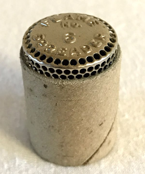 Close-up of a cylindrical wire mesh and cardboard fuse with engraved text on metal top.