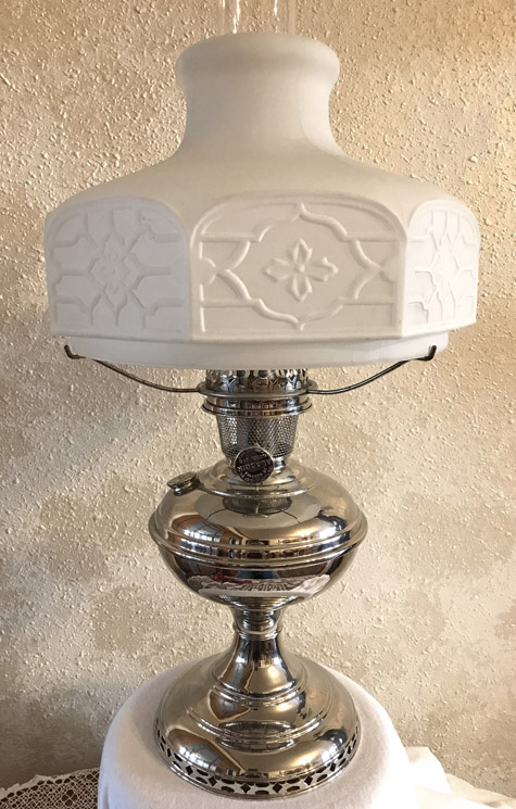 Antique-style oil lamp with ornate white glass shade and shiny silver base on a white cloth.