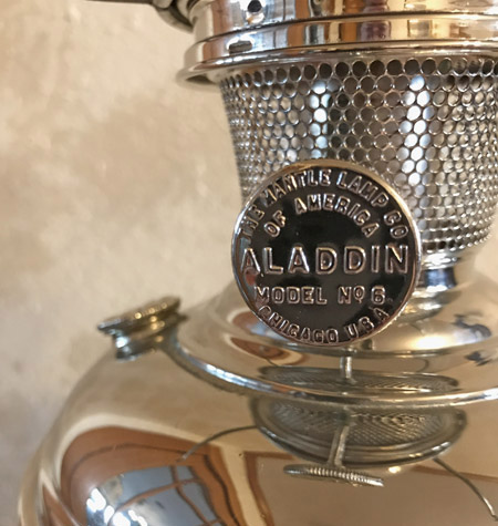 Close-up of a shiny Aladdin Model No. 6 mantle lamp with a metal mesh chimney.