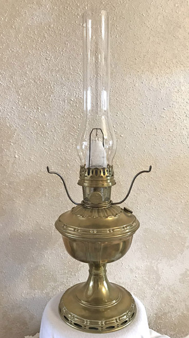 Vintage brass oil lamp with tall clear glass chimney on a white cloth-covered surface.