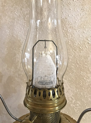 Close-up of a brass oil lamp with a glass chimney and a white fabric wick inside.