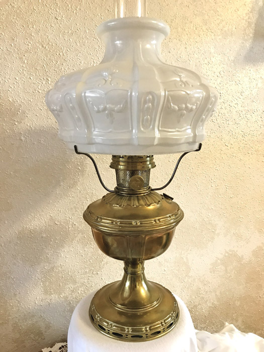 Antique brass oil lamp with ornate frosted glass shade on a white cloth-covered surface.