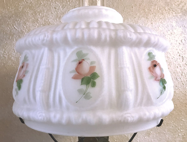 White glass lamp shade with pink rose designs and green leaves on a textured wall background.